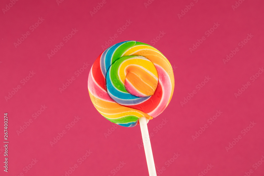 Lollipop, Big Round Rainbow colored lollipop isolated on dark pink Red background Lollipop, Big Round Rainbow colored lollipop isolated on dark pink Red background