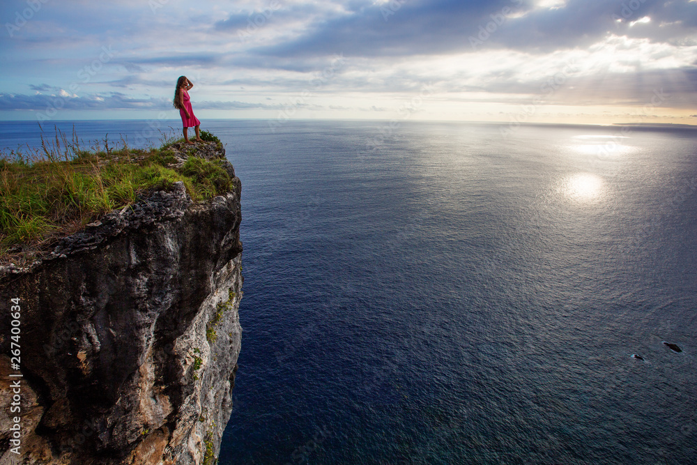 woman sitting on the edge of a cliff and looking at sunset, Nusa Penida woman sitting on the edge of a cliff and looking at sunset, Nusa Penida