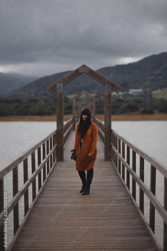 Brunette woman photographer with orange trench coat on a bridge