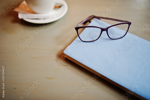 Close up photo of notebook with glasses against cup of coffe at cafe table. Eyewear concept.