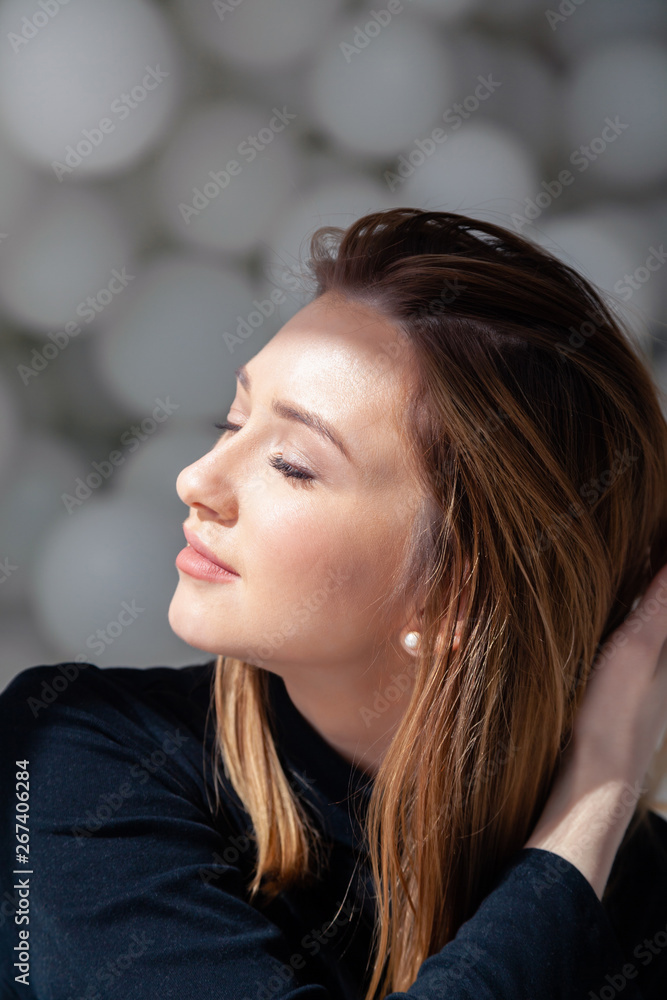 Cute beautiful pretty attractive romantic girl in black sweater turn head to side, close eyes, female beauty portrait with makeup in rays of sun on background of white balloons in photo studio Cute beautiful pretty attractive romantic girl in black sweater turn head to side, close eyes, female beauty portrait with makeup in rays of sun on background of white balloons in photo studio
