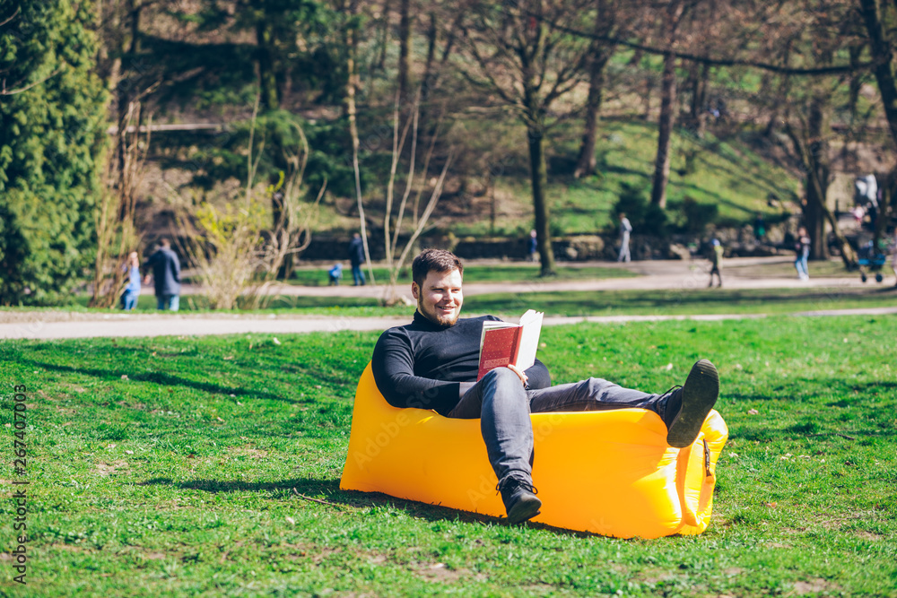 Fototapeta premium book reading concept. man in city park on inflatable mattress