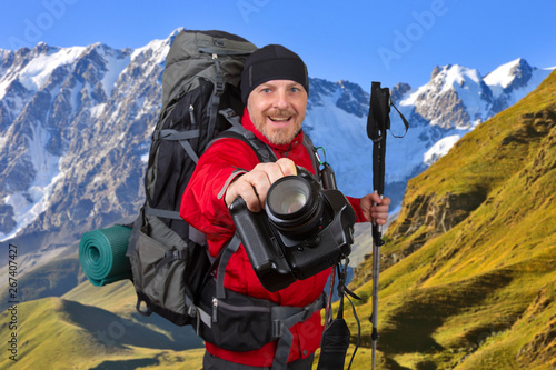 happy traveler with a camera and trekking poles in his hands on the background of the mountains