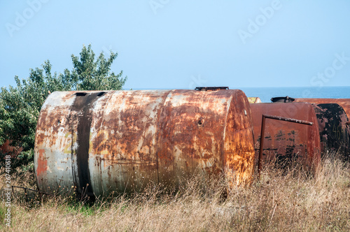 Old abandoned weathered aged corroded fuel tanks on seashore landscape in clear sunny summer day 