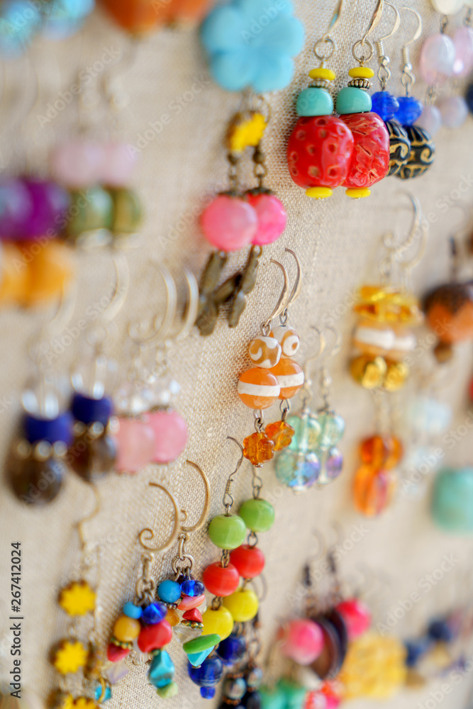 Many colorful earrings for sale at outside street market hanging on canvas, side view, vertical