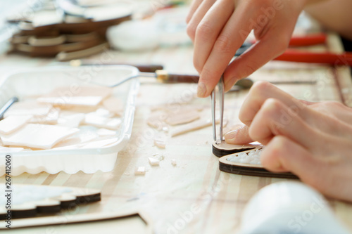 The artist maker mosaic in a wooden harvesting. Female hands closeup collect mosaic of colored stones. Human activity to workplace