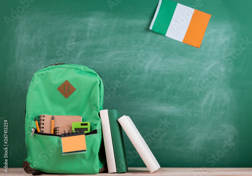 green backpack, flag of the Ireland, books and notebooks on the background of the blackboard
