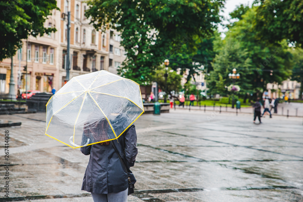 woman walking by wet rainy streets under transparent umbrella