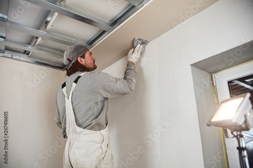 Workman plastering gypsum walls inside the house. © astrosystem