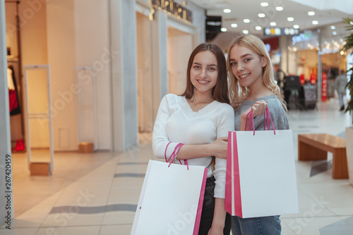 Two charming female shoppers enjoying seasonal sales at local shopping mall, copy space. Attractive happy women smiling, holding shopping bags. Sales, consumptions concept