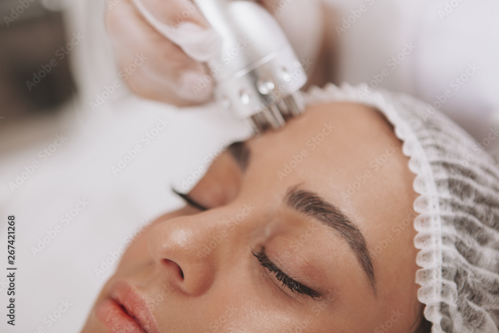 Cropped close up of a beautiful woman getting facial treatment at beauty clinic. Cosmetologist using hardware skincare equipment. Beautician performing microcurrent therapy on female patient