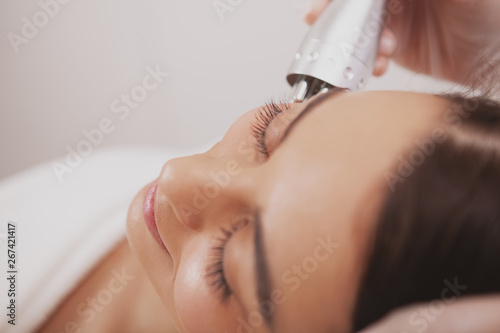 Obraz na plátně Top view cropped close up of a beautiful woman smiling, getting facial hardware treatment at beauty clinic