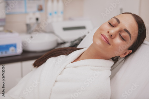 Charming beautiful young woman relaxing at cosmetology clinic after skincare treatment. Attractive female patient with perfect healthy glowing skin resting at beauty salon, copy space