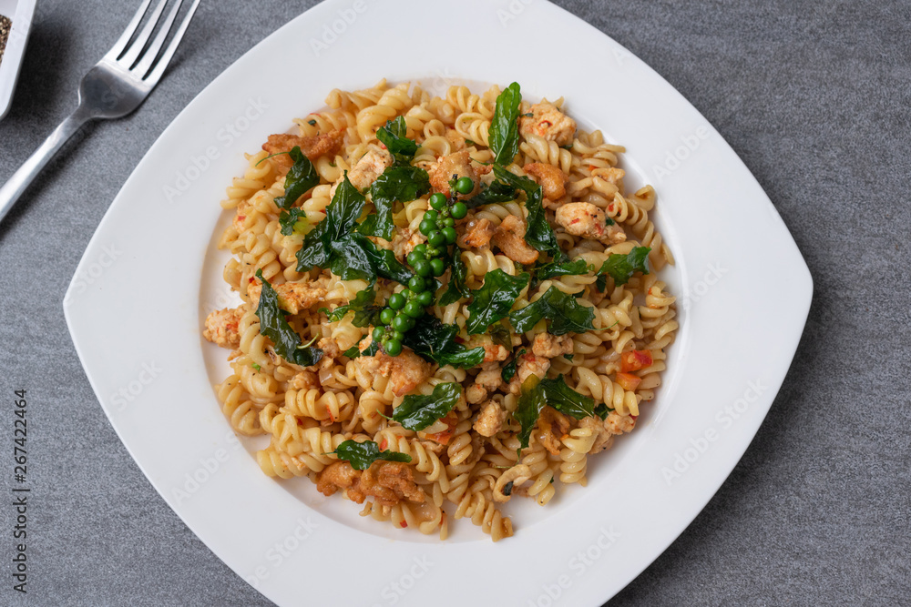 Spiral pasta in fried basil with chicken in white dish on concrete table. Spiral pasta in fried basil with chicken in white dish on concrete table.