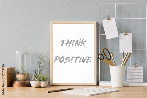 Home interior of creative desk with mock up photo frame on the brown wooden table with office accesories, tillandsia in design pots, notebook and notes. Grey walls. Minimal concept of mockup.