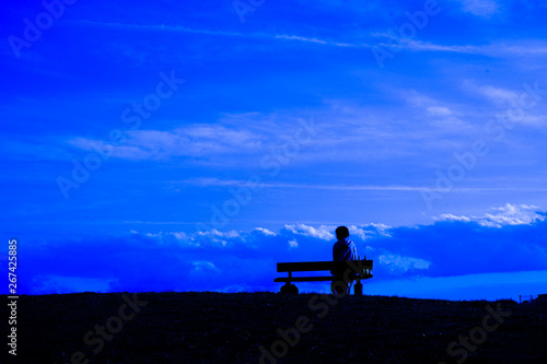 夕焼けの丘に座る女性のシルエットと星空
