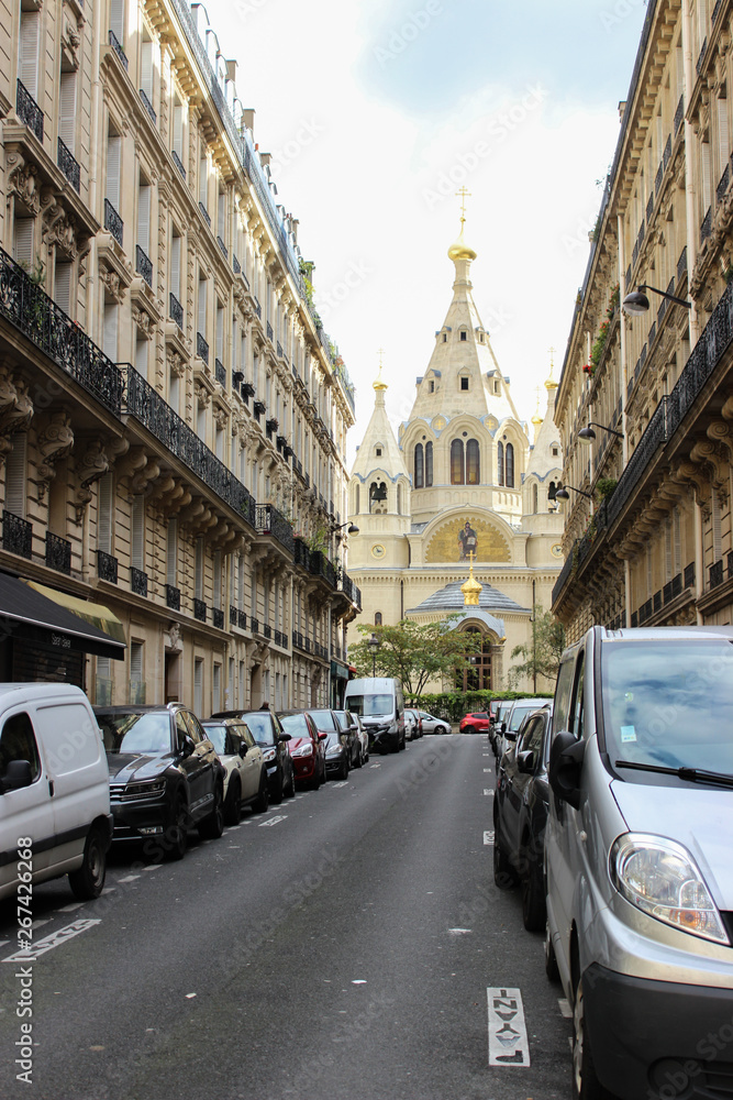 Paris street with beautiful houses in the old architectural style. Buildings with wrought iron balconies and wooden shutters.At the end of the street Cathedral.Cars are parked on the side of the road.