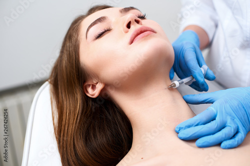 Beautician doctor with botulinum toxin syringe making injection to platysmal bands. Neck rejuvenation mesotherapy. Anti-aging treatment and face lift in cosmetology clinic. Patient lying on chair.