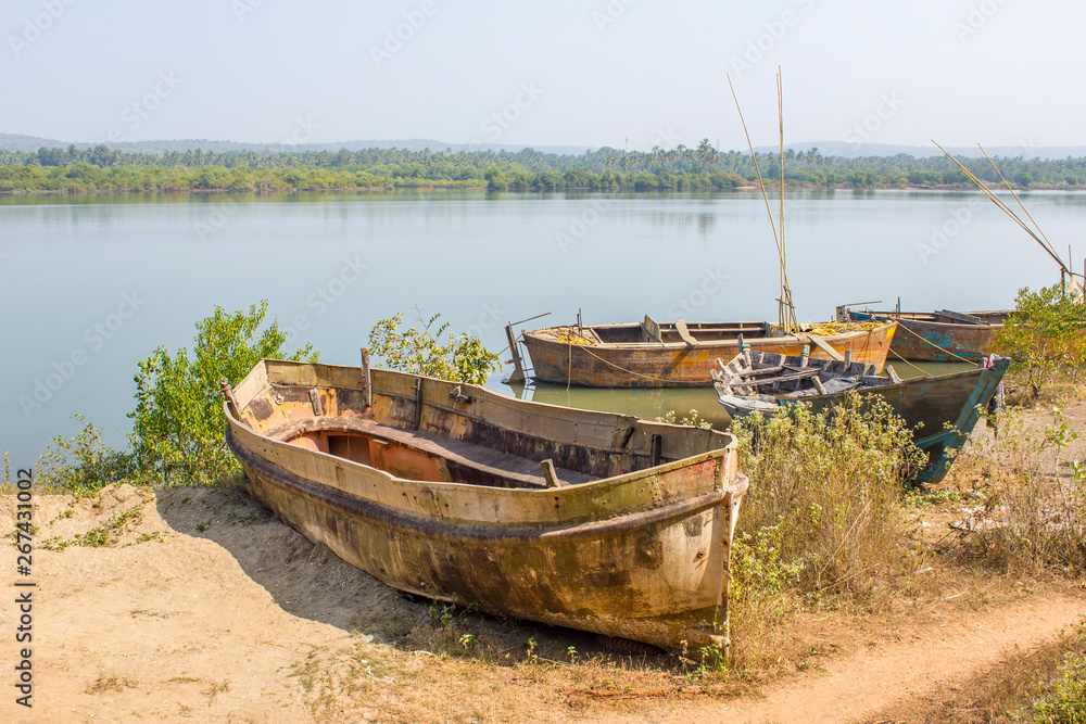 old broken and abandoned boats on the shore against the backdrop of the river and the green forest