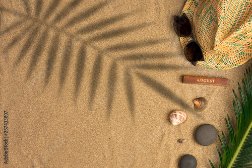 Stylish summer composition with green leaves, hat and sunglasses on a sand background with shadows. Artwork mockup with copy space