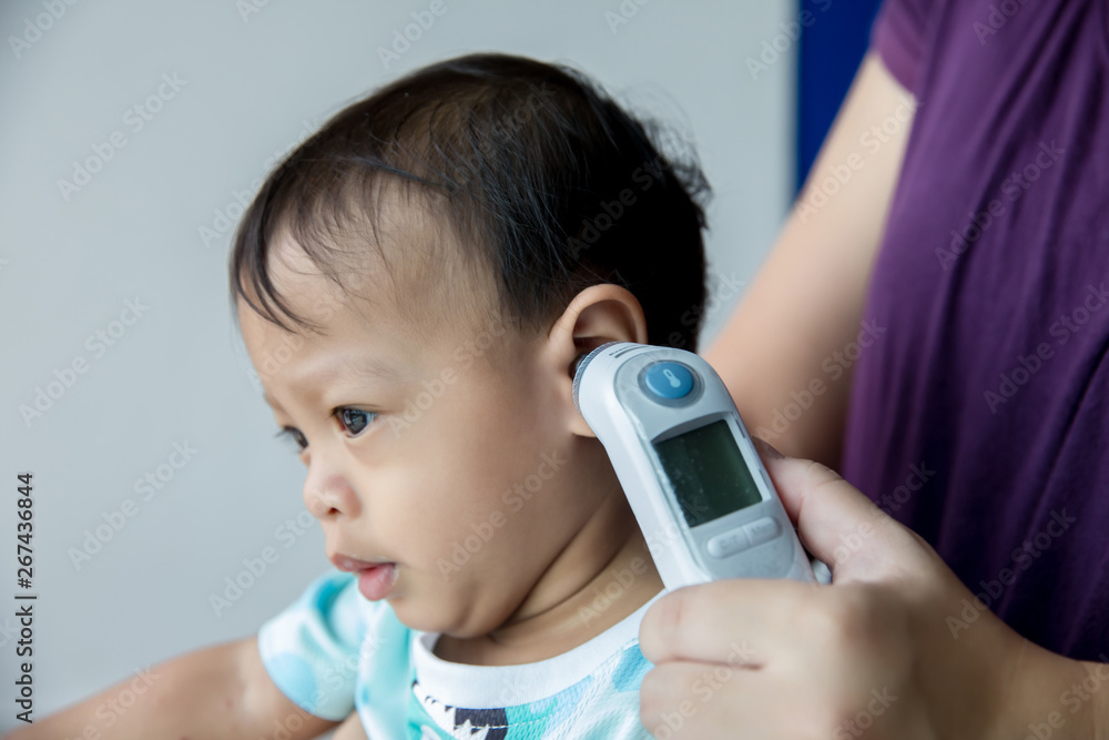 Doctor measuring temperature cute baby boy at hospital . Mother takes
