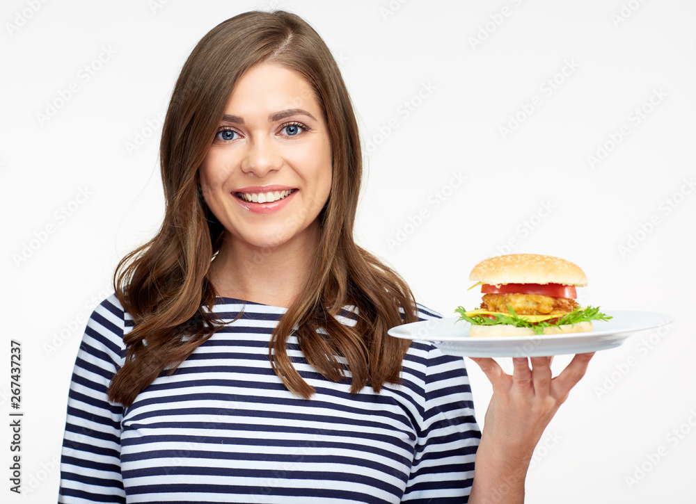 Smiling woman holding burger on white plate.