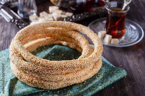 Taste Simit turkish bagels on a green napkin next to hot turkish tea glass and sugar on a wooden table on dark background, closeup