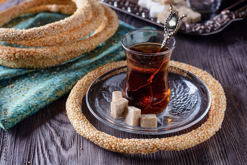 Taste Simit turkish bagels on a green napkin next to hot turkish tea glass and sugar on a wooden table on dark background