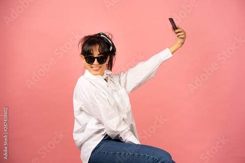Young girl in sunglasses making selfie on a pink background.
