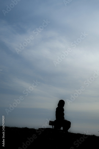 夕焼けの丘に座る女性のシルエット © kanzilyou
