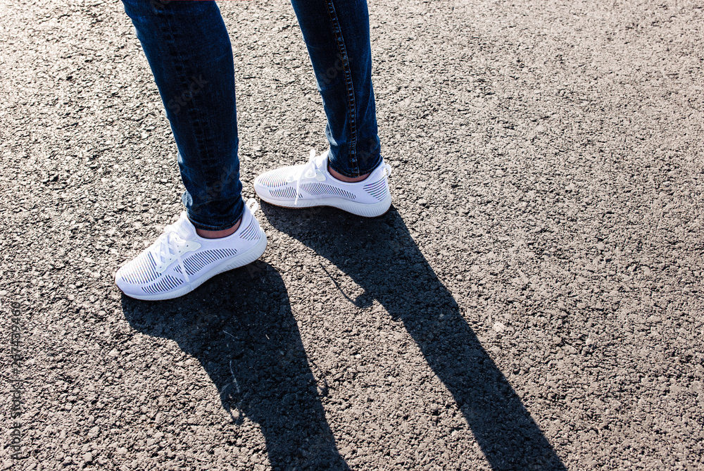 Woman in white sneakers standing on asphalt road towards sun, close up