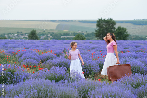 young woman and girl are walking through the lavender flower field, beautiful summer landscape