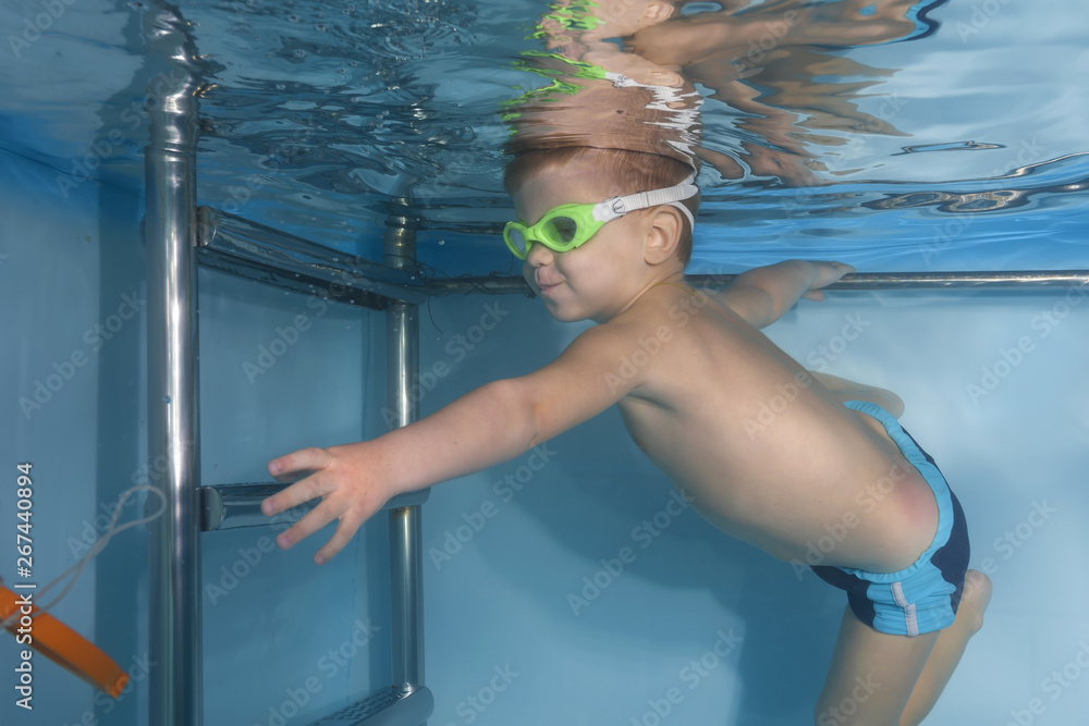 Boy in glasses plays with a toy under water in the pool. Healthy family lifestyle and children water sports activity. Child development, disease prevention