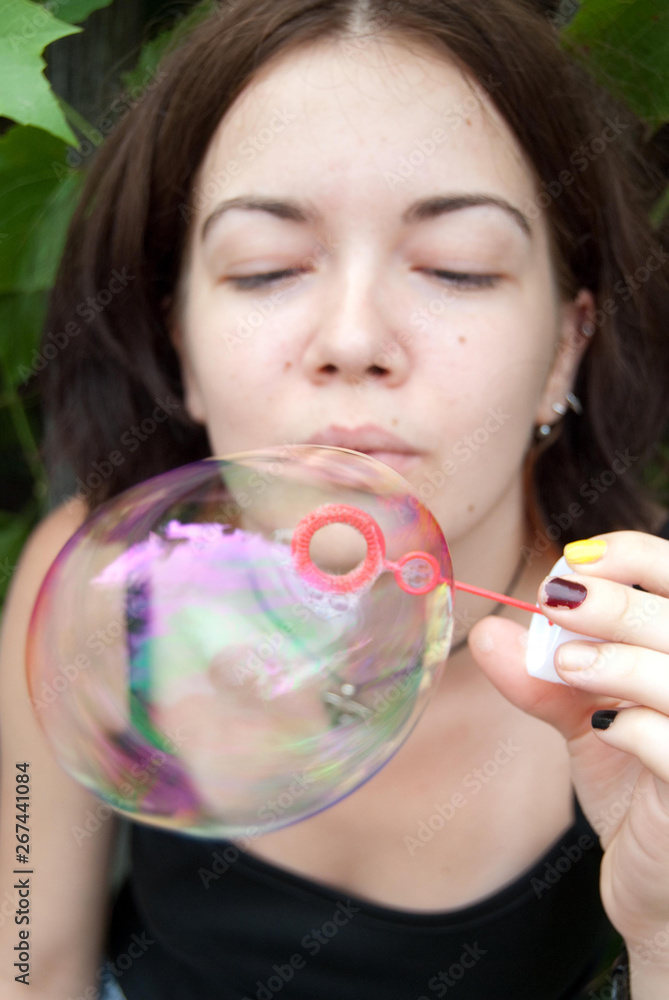 Girl playing childish popping soap balloons out of a straw on a hot summer day