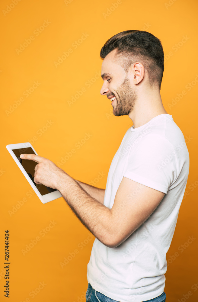 Side view portrait of casual business man with modern tablet in hands over yellow background Side view portrait of casual business man with modern tablet in hands over yellow background