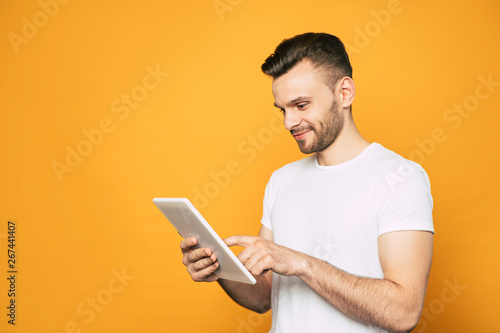 Side view portrait of casual business man with modern tablet in hands over yellow background