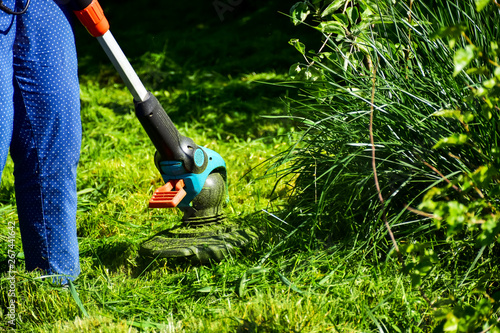 The simple mThoments of life, ordinary work in the garden -  man trimming grass with heavy-duty trimmer in the garden, suitable for trimming long lawn edges and larger hard-to-access areas. Man mows .