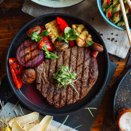 Beef steak with a side dish of grilled vegetables, with natural light from the window on a wooden table, BBQ