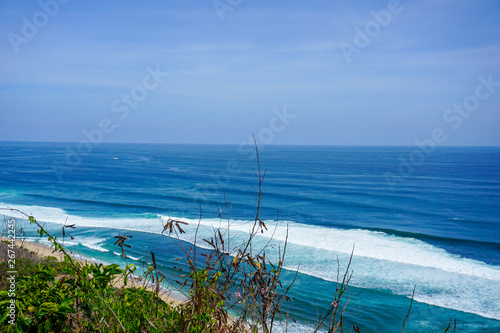 Blue sky and waves crashing onto the beach the Uluwatu Temple in Bali, Indonesia.