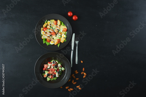 Caesar and Greek salads on a dark background. Top view with place for save pasta.