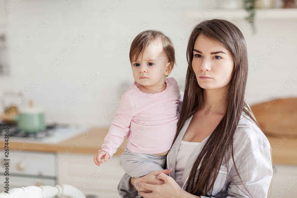 Portrait of determined serious mother holding baby daughter in kicthen, copy space to the left Portrait of determined serious mother holding baby daughter in kicthen, copy space to the left
