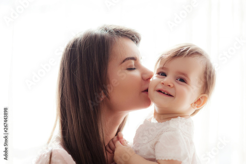 Beautiful portrait of loving mother with closed eyes kissing her happy smiling baby daughter on cheek