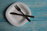 White blank plate, fork and knife, lay on a blue wooden background.