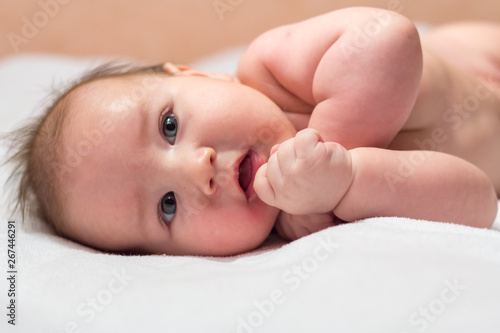 Newborn baby lying on its side and smiling on a white sheet and looking up
