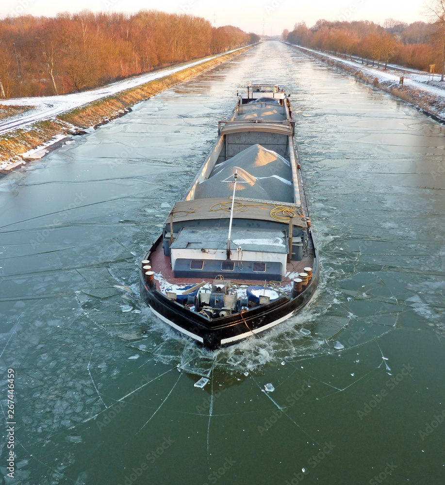 A barge transporting material sailing on a small frozen canal