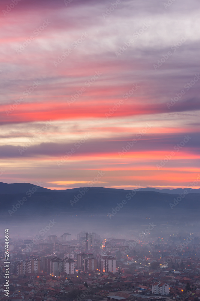 Unreal, purple sunset sky above night cityscape with city lights covered by thick mist