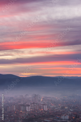 Unreal  purple sunset sky above night cityscape with city lights covered by thick mist