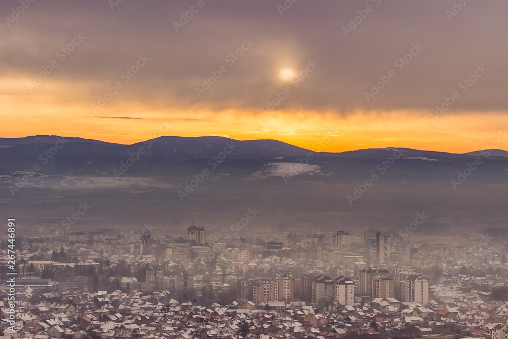 Beautiful view of misty Pirot cityscape covered by first winter snow and stunning golden sunset colors in the sky
