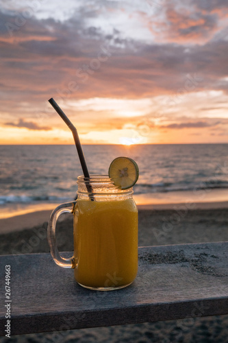 Close up of glass of colorful fruit shakes on background of tropical beach at sunset in the evening