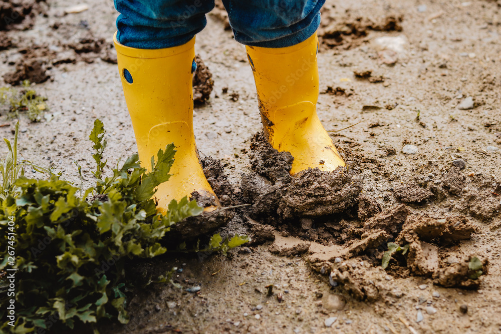 Child legs in yellow muddy rubber boots on wet mud. Baby playing with dirt  at rainy weather. Gardening at spring, weather concept Stock Photo | Adobe  Stock